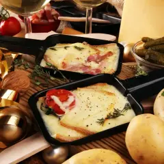 Comment présenter une raclette : fromage fondu, pommes de terre, cornichons et charcuterie, le tout prêt à être dégusté.