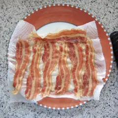 Fertig gegrillter Bacon auf Küchenpapier auf einem Teller. Schnell und einfach in der Mikrowelle zubereitet.