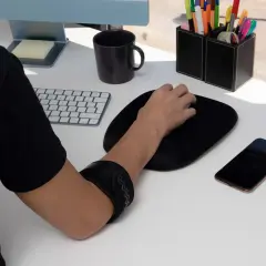 Braccio con tutore per alleviare il dolore mano mouse. Tastiera, mouse, telefono e pianta sul tavolo.