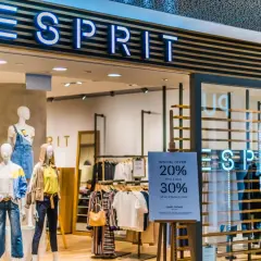 Sklep Esprit z neonowym logo. Manekiny prezentują letnie ubrania, a obok widoczna jest tablica z promocją.