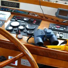 Un binocolo da ingrandimento, pronto per scrutare l'orizzonte, riposa sul cruscotto di una barca, accanto a strumenti di navigazione e a un timone in legno lucido.