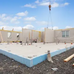 Budowa domu z prefabrykatów. Widać fundament z keramzytobetonu, ściany zewnętrzne i pracującą na budowie żuraw.