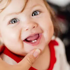 Ein Baby lächelt stolz und zeigt seinen ersten Zahn.