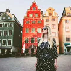 En kvinna med solglasögon står framför färgglada hus på ett torg. Kanske är detta sveriges vackraste stad.