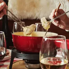 Des mains plongent des morceaux de pain dans une fondue pyrénéenne crémeuse, un moment convivial autour d'un plat réconfortant.