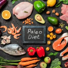 Na czarnej tablicy napis "Paleo Diet". Wokół świeże ryby, mięso, owoce, warzywa i orzechy – składniki diety paleo.