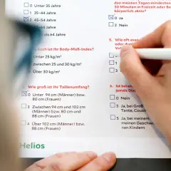 Hand füllt Fragebogen aus, der Fragen zu Lebensstil und Risikofaktoren für Diabetes enthält. Eine Diabetes Blutwerte Tabelle ist Teil des Dokuments.