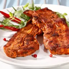 Dwa soczyste kawałki **boczku na grilla**, przyprawione i ozdobione papryczkami chili oraz zielonymi listkami.