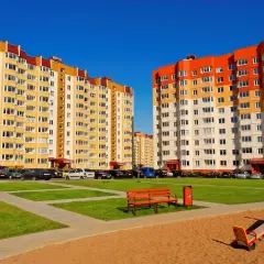 Dwa bloki z wielkiej płyty, jeden żółty, drugi pomarańczowo-biały, stoją na tle błękitnego nieba.