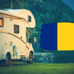 Kamper na trawie, z widokiem na jezioro i góry. Obok flaga Rumunii. Idealne miejsce na podróż kamperem po Rumunii.
