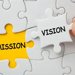 Dłoń dopasowuje element układanki z napisem "VISION" do pola z napisem "MISSION", symbolizując wizję firmy.