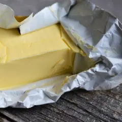 Kostka masła w folii aluminiowej na drewnianym blacie. Zastanawiasz się, czy można jeść przeterminowane masło?
