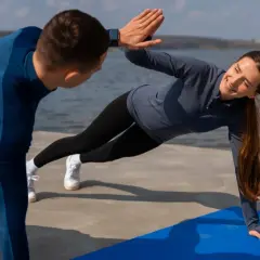 Para ćwiczy na macie nad wodą, wykonując boczne deski i dając sobie high five. Idealny sport dla par.