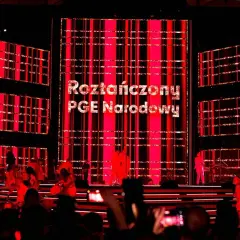Roztańczony PGE Narodowy rozświetlony czerwienią. Na scenie artyści, w tle wielkie ekrany z napisem.