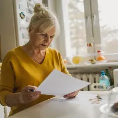 Starsza pani, jak mama 4 plus, analizuje rachunki przy kuchennym stole.