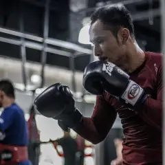 A boxer, sweating and focused, throws a powerful southpaw jab at a heavy bag in a dimly lit gym.
