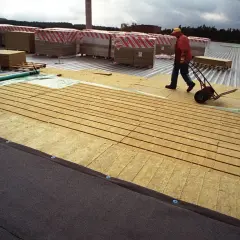 Budowa dachu płaskiego: pracownik z wózkiem transportuje materiały izolacyjne na budowie.