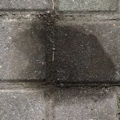 Stare plamy z oleju na kostce brukowej tworzą ciemny, rozlany kształt, świadcząc o dawnych wyciekach.