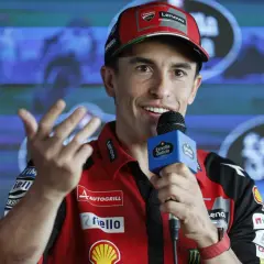 Marc Márquez, con su gorra roja y polo de Ducati, habla con un micrófono. Su edad se refleja en su energía y sonrisa.