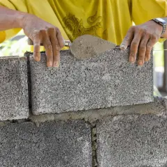 Murarz układa bloczek betonowy, sprawdzając jego wymiary.
