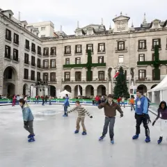 Gente patinando en la pista de hielo de Santander, con un árbol de Navidad y edificios históricos de fondo.