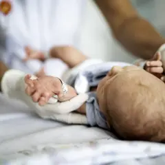Delikatne badania neurologiczne noworodka. Ręce w rękawiczkach badają maleńkie dłonie i stopy dziecka.