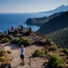 Un hombre toma una foto en un mirador con vistas a la cala de enmedio y montañas.