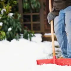 Mann schaufelt Schnee, um dem Winterdienst-Gesetz nachzukommen.