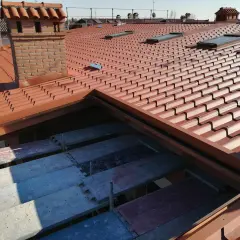 Tetto alla piemontese con tegole rosse, comignoli in mattoni e lucernari. In primo piano, impalcature per lavori di ristrutturazione.