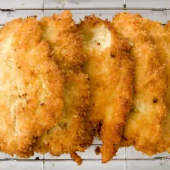 Fileteadas pechugas de pollo empanadas, doradas y crujientes, reposan sobre una rejilla metálica.