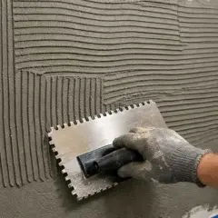 Main tenant, une truelle dentée pour étaler la colle carrelage préparée sur un mur. Les sillons créés par la truelle sont visibles.