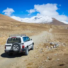 Biały SUV na drodze gruntowej, w tle góry pokryte śniegiem. Przygoda na Pamir Highway.