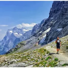 Turystka wędruje ścieżką u podnóża potężnego Eiger szczytu. W tle majestatyczne, ośnieżone góry i błękitne niebo.