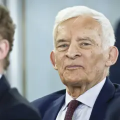 Jerzy Buzek, w otoczeniu innych mężczyzn, z uwagą słucha przemówienia.
