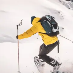 Person en raquettes, veste jaune vif, explorant un paysage enneigé. Les bâtons de randonnée aident à progresser dans la poudreuse.