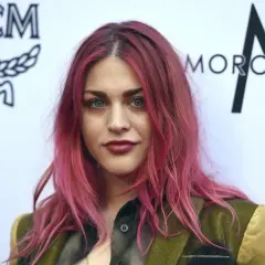 Frances Bean Cobain z różowymi włosami i w zielonej marynarce pozuje na tle logo MCM.