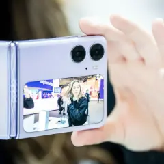 Osoba robi selfie na wystawie, korzystając z dobrego aparatu w telefonie. Na ekranie widać młodą kobietę.