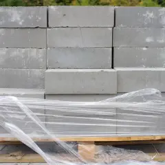 Ułożone na palecie bloczki betonowe, owinięte folią. Widać ich standardowe bloczek betonowy wymiary, gotowe do budowy.
