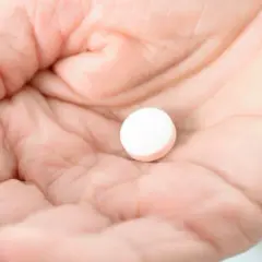 Dłoń trzyma białą tabletkę, być może Vicodin, która ma sfinansować ulgę w bólu.
