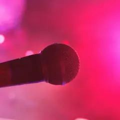 Mikrofon na scenie, gotowy na śpiew bez tekstu. Różowe światła tworzą magiczną atmosferę.