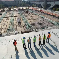 Grupa budowlańców w kaskach i kamizelkach odblaskowych omawia postęp prac na budowie, zgodnie z art. 62 prawa budowlanego.