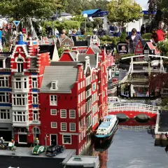 Miniaturowa holenderska zabudowa z kanałami i mostami w **Lego Land**. Ludzie spacerują wśród kolorowych budynków z klocków.
