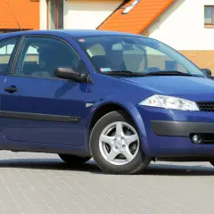 Niebieski Renault Megane 2 hatchback stoi na brukowanym podjeździe przed domem.