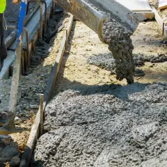 Betoniarka wylewa beton na plac budowy. Pracownik w kamizelce i spodniach przygotowuje teren. Zastanawiasz się, ile kosztuje kubik betonu?