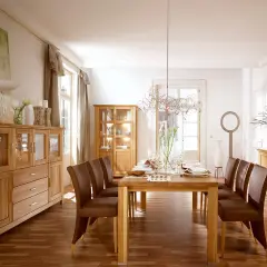 Nowoczesny salon ze starymi meblami z litego drewna. Dębowe komody i witryny tworzą ciepłą atmosferę, a skórzane krzesła przy drewnianym stole zapraszają do wspólnego posiłku.