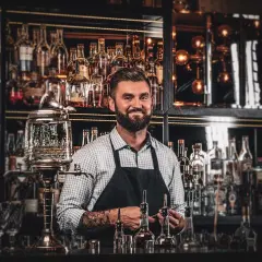 Barman z tatuażami prezentuje akcesoria do przygotowania absyntu. Poznaj tajniki, jak pić absynt, by w pełni docenić jego smak.