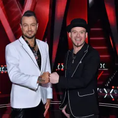 Baron i Tomson, dwaj mężczyźni w eleganckich strojach, pozdrawiają się na tle sceny.