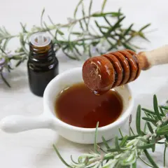 Un vasetto di vetro scuro, un cucchiaio di miele che cola e rametti di rosmarino fresco: ingredienti per un estratto di rosmarino fai da te.