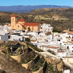 Vista panorámica de Lucainena de las Torres, un pueblo blanco andaluz con una iglesia de tejado naranja y montañas al fondo. ¡Un lugar con mucho que ver!
