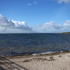 Plaża z piaskiem i morzem, na którym wielu kitesurferów korzysta z wiatru. Idealne miejsce, gdzie najcieplej nad morzem, by uprawiać sporty wodne.